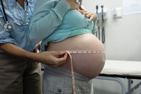 Mid section of Caucasian female doctor measuring pregnant woman belly in examination room at...