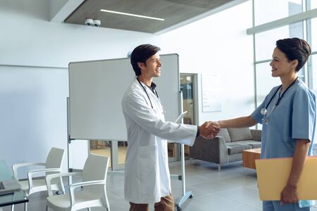 Side view of male happy Caucasian doctor shaking hands with smiling female Caucasian nurse in the...