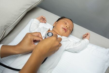 Close-up of Caucasian female doctor examining baby with stethoscope on table of medical examination...