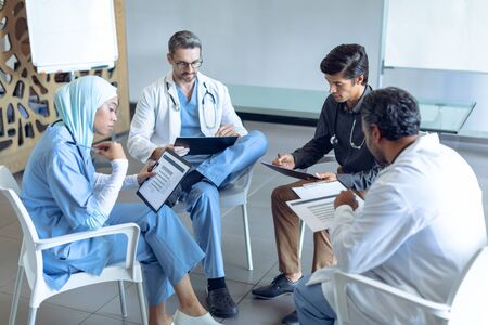 Side view of diverse medical team with stethoscopes around the neck reading documents together in the hospital.の写真素材