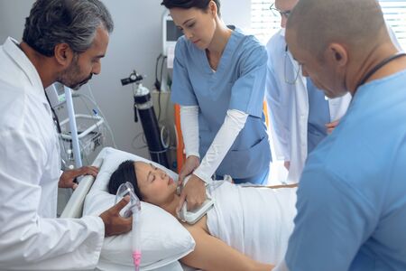 Side view of diverse doctors using defibrillator on Asian female patient in ward at hospitalの写真素材