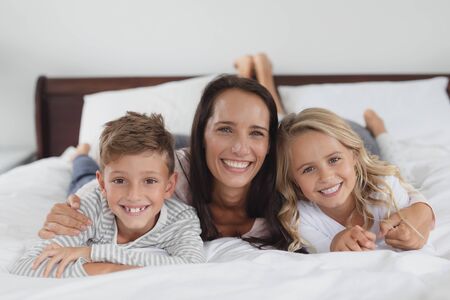 Portrait of Caucasian mother and children lying together on bed in bedroom at homeの写真素材