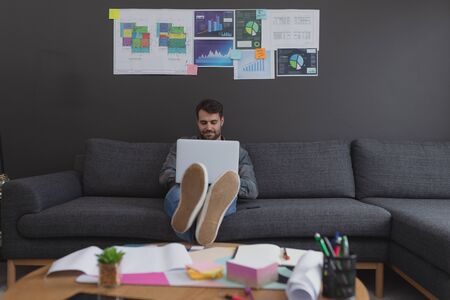 Front view of Caucasian male executive working on laptop on sofa in officeの写真素材