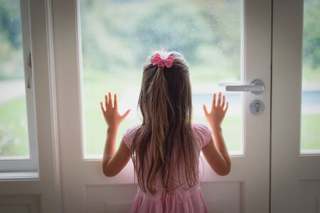 Rear view of Caucasian girl looking through window at homeの写真素材