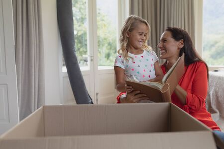 Front view of Caucasian mother and daughter reading a story book in living room at homeの写真素材