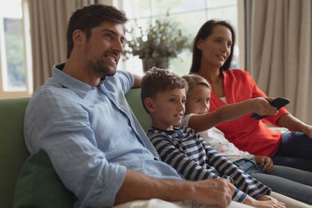 Side view of happy Caucasian family watching television in living room at home