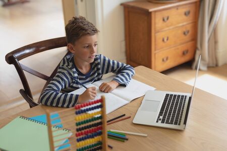 High angle view of Caucasian boy doing homework at table in a comfortable homeの写真素材