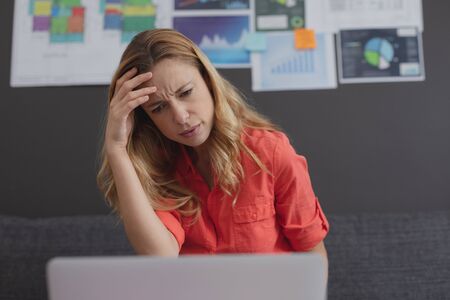 Front view of tensed Caucasian female executive working on laptop while sitting on sofa in office