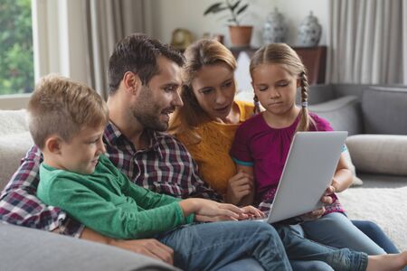 Side view of caucasian family using laptop on the sofa in a comfortable homeの写真素材