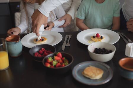 Mid section of Caucasian father putting cream on pancake at dining table in a comfortable homeの写真素材