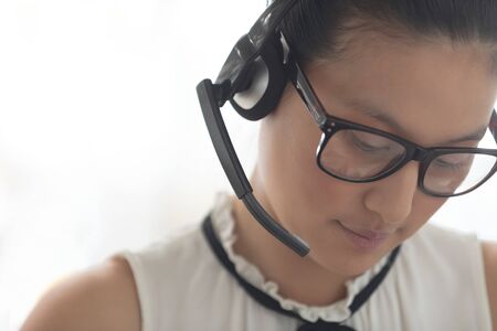 Front view of beautiful Asian female customer service executive with headset looking down in a modern officeの写真素材
