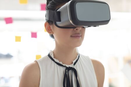 Front view of Asian female executive using virtual reality headset in a modern office