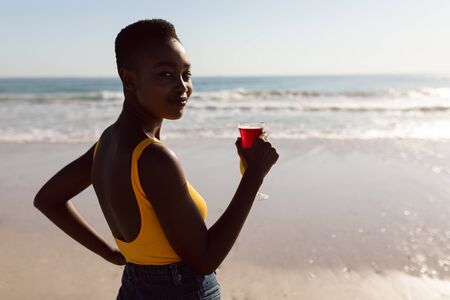 Portrait of African-american woman with cocktail drink standing on the beachの写真素材