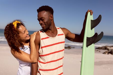 Front view of happy young Mixed-race couple with surfboard looking each other on beach in the sunshineの写真素材