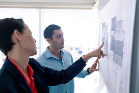 Side view of Caucasian architects discussing over blueprint on glass board in a modern officeの写真素材
