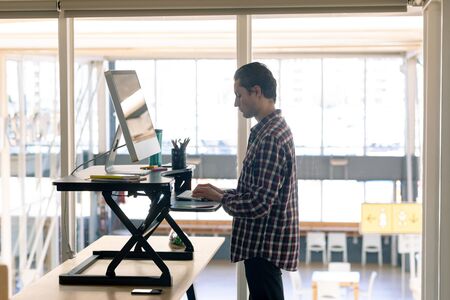 Side view of Caucasian male graphic designer working on computer at desk in officeの写真素材