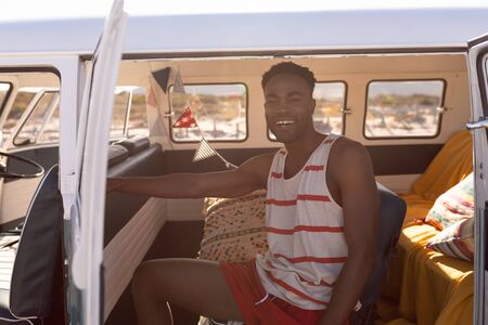 front view of happy young African-american man sitting in camper van at beach