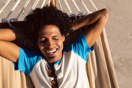 Front view of happy African-american man sleeping in a hammock on the beachの写真素材