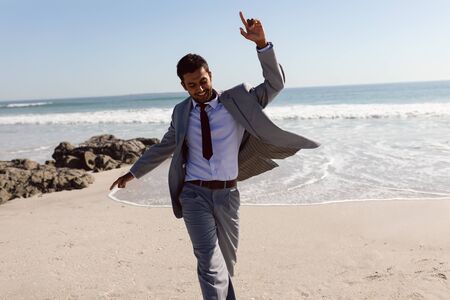 Front view of happy young Mixed-race Businessman dancing on the beachの写真素材