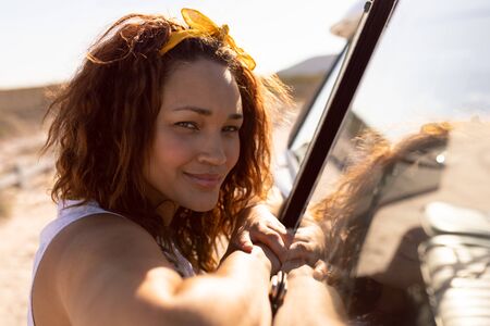 Side view of beautiful young Mixed-race woman leaning on camper van at beach