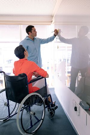 Side view of Caucasian business executives discussing over glass board in a modern office. Disabled female executive sitting in wheelchair.の写真素材