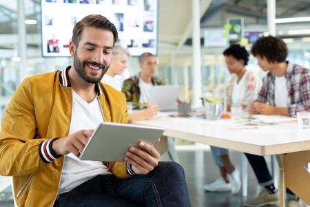 Front view of Caucasian male fashion designer using digital tablet while diverse business people...