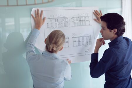 Rear view of Caucasian male and female architects discussing over blueprint in office