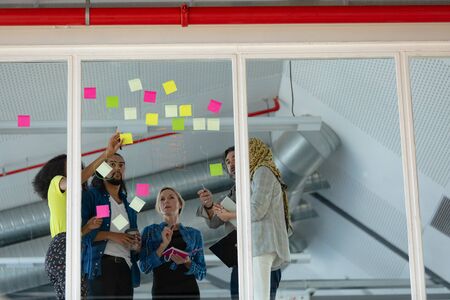 Low angle view of diverse business people discussing over sticky notes on glass wall in a modern...