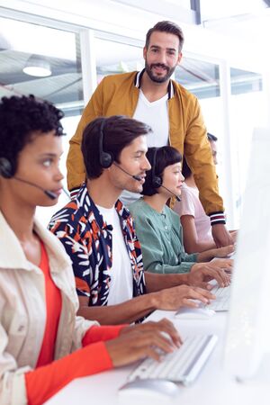 Side view of diverse customer service executive trainer assisting her team at desk in officeの写真素材