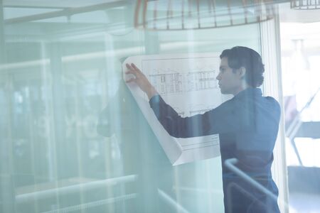 Rear view of Caucasian male architect looking at blueprint in officeの写真素材
