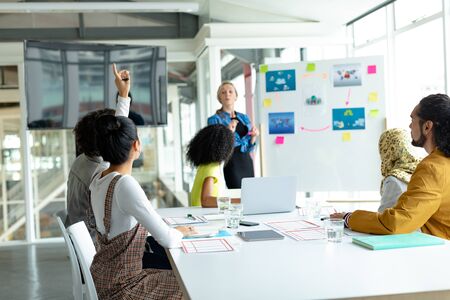 Side view of Mixed-raced businesswoman raising hand in presentation during meeting in a modern officeの写真素材