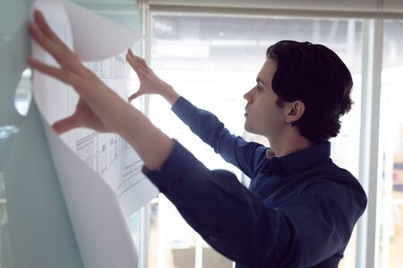 Side view of Caucasian male architect looking at blueprint in office