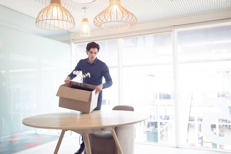 Front view of smart Caucasian male executive holding cardboard box with plant in office