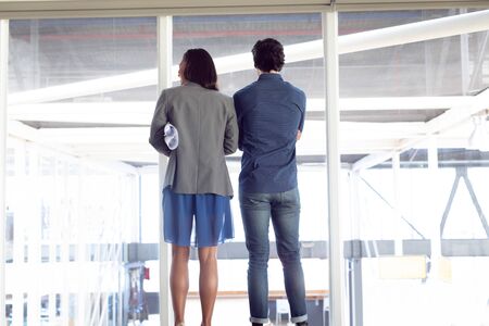 Rear view of diverse male and female architects looking through window in office
