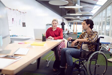 Side view of Caucasian male and female fashion designers interacting with each other at desk in officeの写真素材