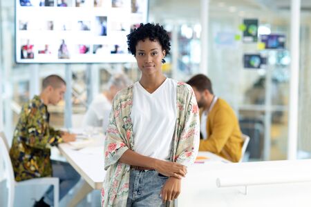Portrait of African american female fashion designer leaning on a table at conference room while diverse business people discussing in officeの写真素材