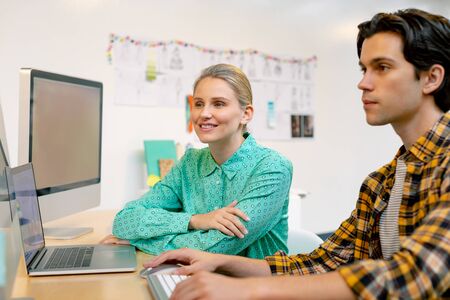 side view of Caucasian male and female executive discussing over computer at desk in officeの写真素材