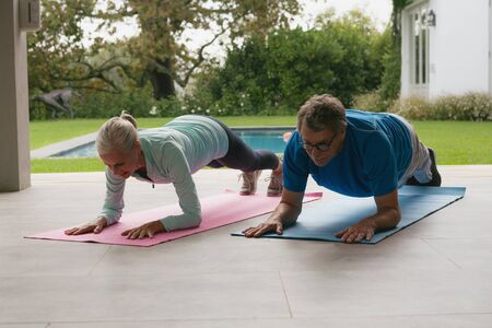 Front view of determined active senior Caucasian couple doing plank exercise in the porch at homeの写真素材