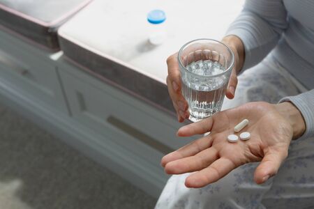 Mid section of active senior Caucasian woman taking medicine in bedroom at homeの写真素材