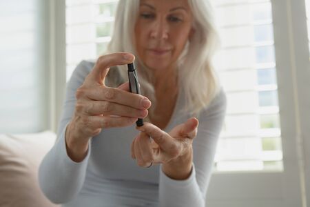 Front view of active senior Caucasian woman testing her blood sugar level with glucometer at home