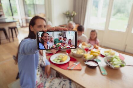 Front view of multi-generation Caucasian family taking selfie with mobile phone while having food on...