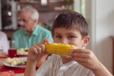 Portrait of Caucasian boy holding maize at dining table at home