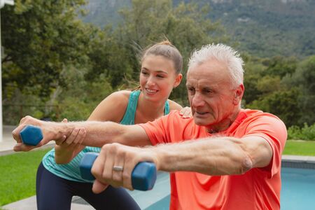 Side view of Caucasian female trainer assisting active senior Caucasian man to exercise with...