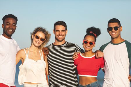 Portrait of diverse happy friends standing together and looking at the camera on the beach