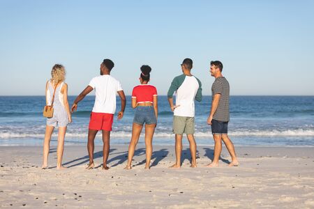 Rear view of diverse friends standing together on the beachの写真素材