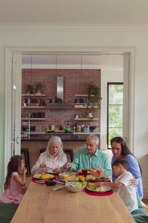Front view of multi-generation Caucasian family having food together on dining table at home