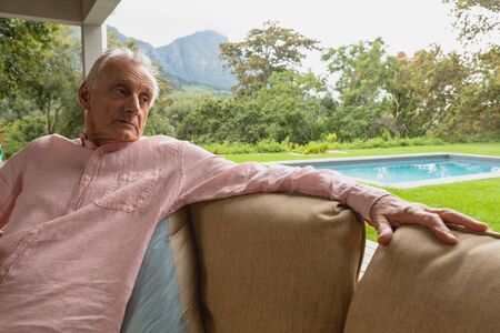 Front view of thoughtful active senior Caucasian man relaxing on sofa in the porch at homeの写真素材