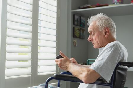 Side view of active senior Caucasian man in wheelchair using mobile phone at homeの写真素材