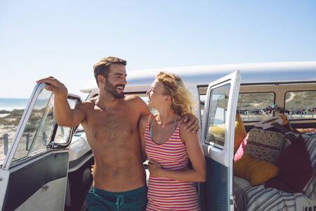 Front view of happy Caucasian couple talking with each other near camper van at beach in the sunshineの写真素材