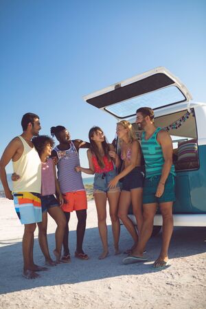 Front view of happy group of diverse friends interacting with each other near camper van at beach